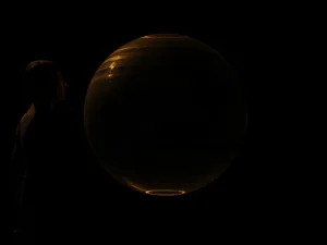 Una figura en una habitación oscura, congelada en medio de un movimiento, mirando una pantalla suspendida.